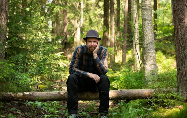 Juha Kauppinen istuu kaatuneen rungon päällä metsässä
